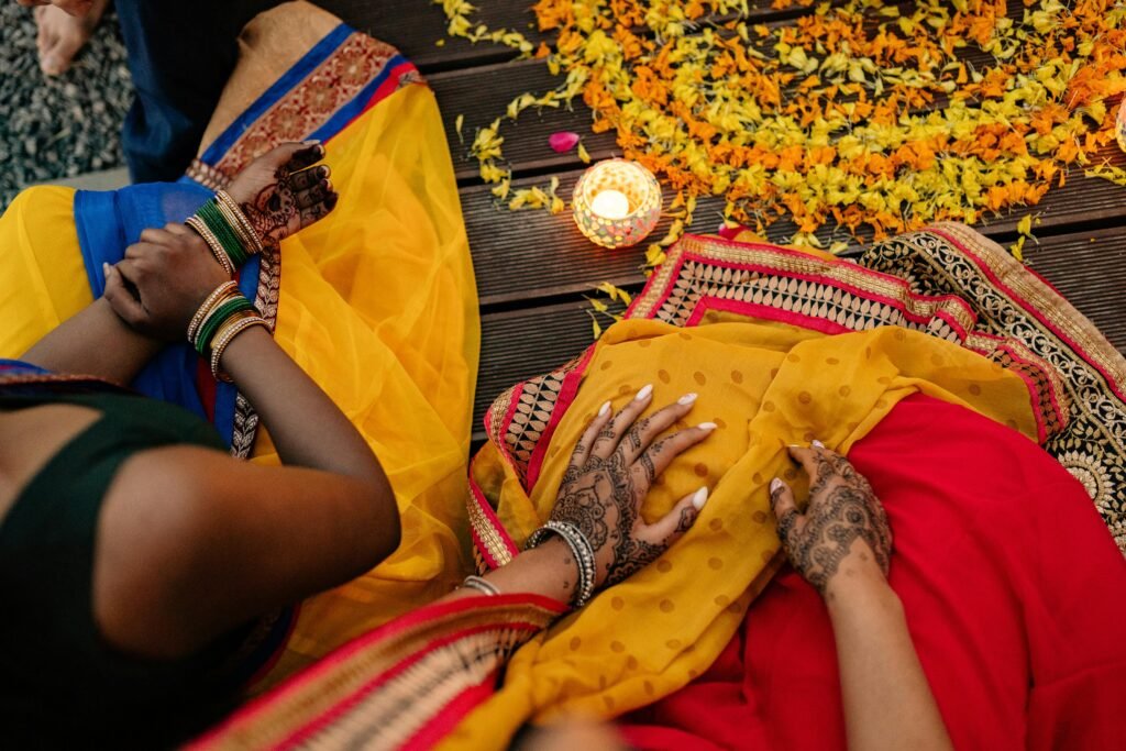 Overhead view of women in saris with mehendi, surrounded by flowers and a candle, highlighting Indian traditions.