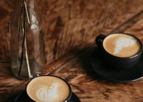 Aesthetic café setting with two cappuccinos on a wooden table and dried flowers.