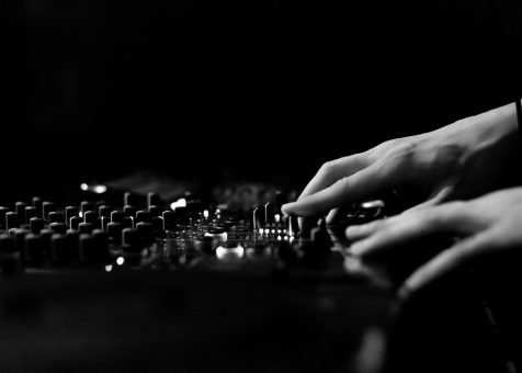 Artistic black and white image of hands adjusting a DJ console in a club.