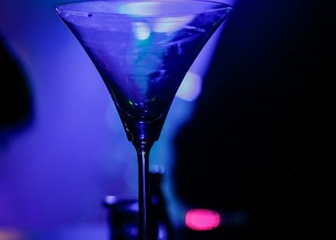 A crystal martini glass glows under vibrant nightclub lighting.